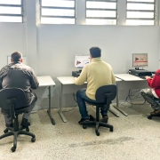 Na foto, três homens estão sentados na frente de computadores