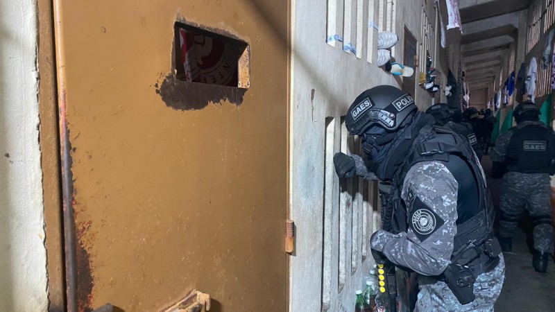 Na foto, um homem com capacete e farda da Polícia Penal  está no corredor da penitenciária 