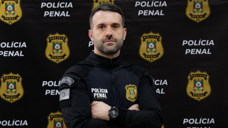 homem fardado em frente a banner da Polícia Penal
