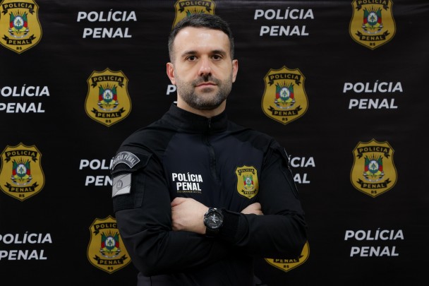 homem fardado em frente a banner da Polícia Penal