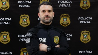 homem fardado em frente a banner da Polícia Penal