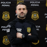 homem fardado em frente a banner da Polícia Penal